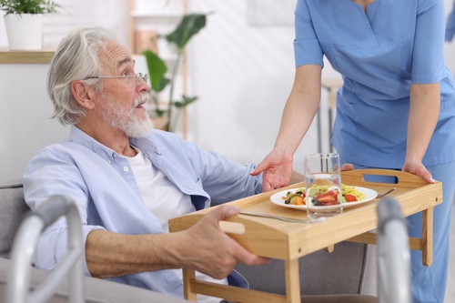 Caregiver serving a meal on a wooden tray to a senior man indoors
