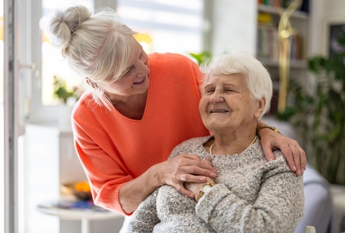 An adult daughter smiling and supporting her elderly mother at home.